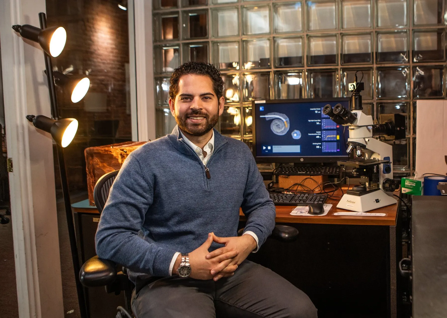 Jay Reddy, photographed by Jim Harris for the Pittsburgh Business Times: at his desk in the Pittsburgh office beside a microscope and a monitor.